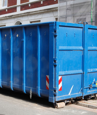 Blaue Absetzmulde für Bauschutt, auf der Straße vor einem Haus mit Baustelle stehend