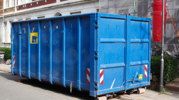Blaue Absetzmulde für Bauschutt, auf der Straße vor einem Haus mit Baustelle stehend