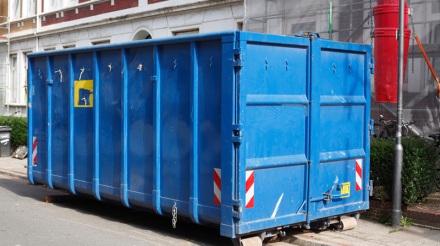 Blaue Absetzmulde für Bauschutt, auf der Straße vor einem Haus mit Baustelle stehend